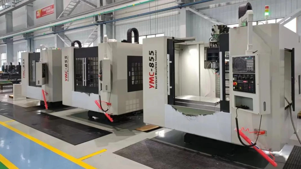 Three white fully enclosed vertical machining centers lined up in a CNC workshop, front operation door open, CNC control panel on the right, with visible worktable and spindle