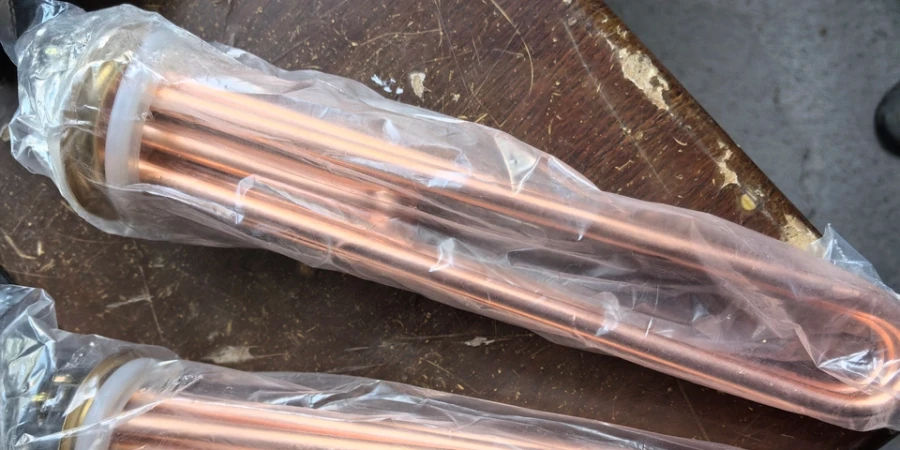 Two copper heating tubes wrapped in clear plastic, resting on a wooden surface.