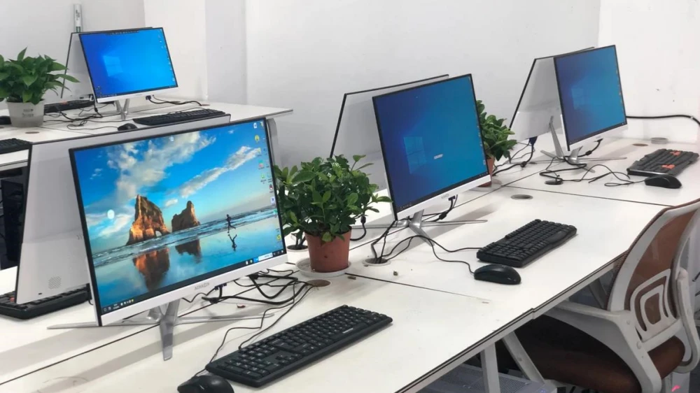 Neatly arranged white all-in-one office computers in a modern workspace, equipped with black keyboards and mice, displaying Windows desktops, illustrating standard employee workstation computer setups.