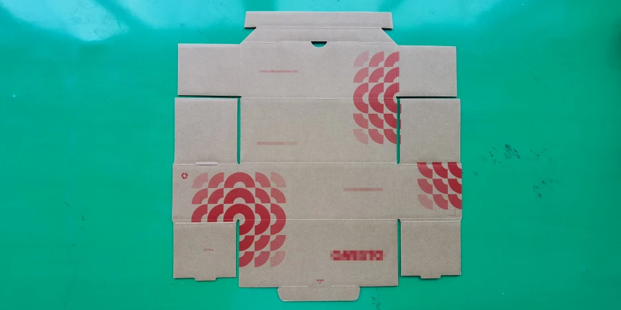 A flat, unfolded brown cardboard inner box with red geometric fan patterns and a red logo, laid on a green surface.