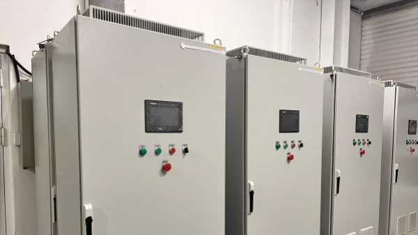 Industrial electrical control panels arranged side by side, light grey metal enclosures with LCD screens and red/green operation buttons on the front panel.