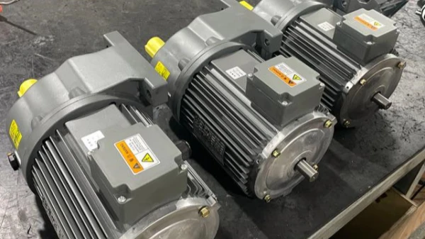 Industrial motors arranged side by side, grey metal housings with cooling fins, top terminal boxes with yellow warning labels.