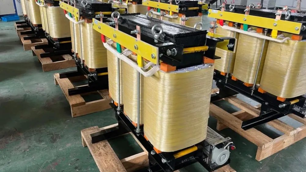 Row of isolation transformer coils with yellow insulation winding, black core and yellow clamps, lifting rings and terminals in a factory
