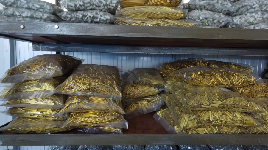 Metal shelves holding clear plastic bags filled with gold-colored and silver-colored metal components used for miniature circuit breakers