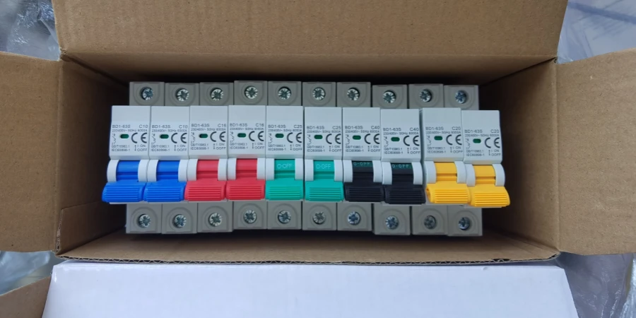 A brown cardboard box holding a row of white circuit breakers featuring blue, red, green, black, and yellow handles.