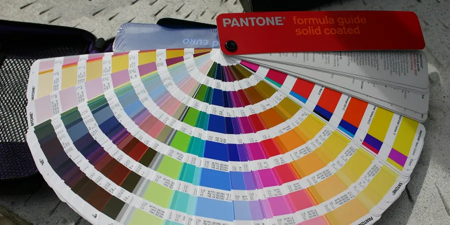 A red PANTONE formula guide solid coated fan deck spread open, showing many color swatches with identification numbers.