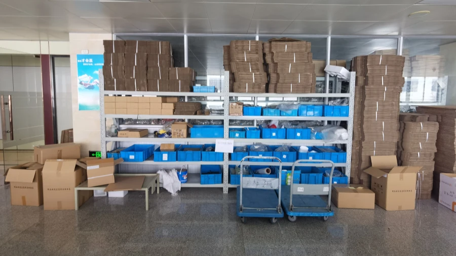 A storage room with metal shelving units holding blue plastic bins and stacked cardboard boxes, with two blue carts on the floor