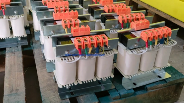 Multiple three-phase dry-type transformers with orange terminal blocks neatly arranged on wooden pallets in a factory workshop, electrical equipment bulk production