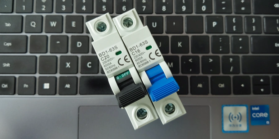 Two white AC miniature circuit breakers with black and blue switches resting on a black laptop keyboard.