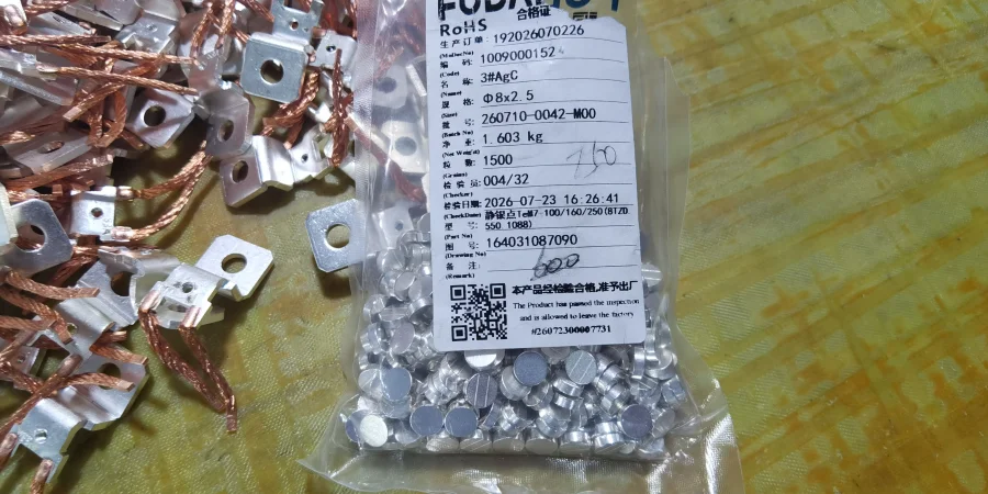 A clear plastic bag filled with small AgC contact discs, with a certificate of conformity attached to the front, next to a pile of braided copper wire pieces with metal ends.