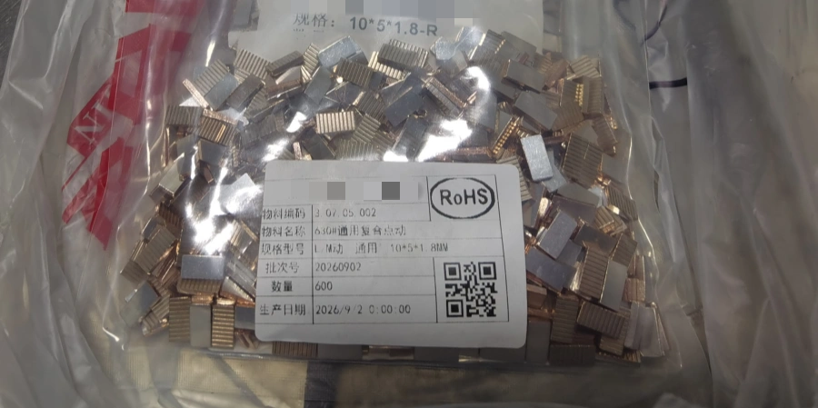 A clear plastic bag filled with rectangular copper-silver composite contact pieces, with a label on the front showing product details, a QR code, and a RoHS mark