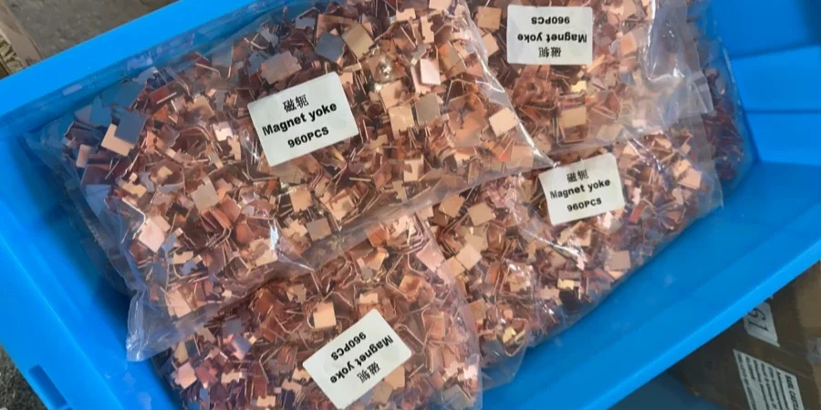 A blue bin holding clear plastic bags filled with copper-colored magnet yokes, each bag labeled 'Magnet yoke 960PCS'.