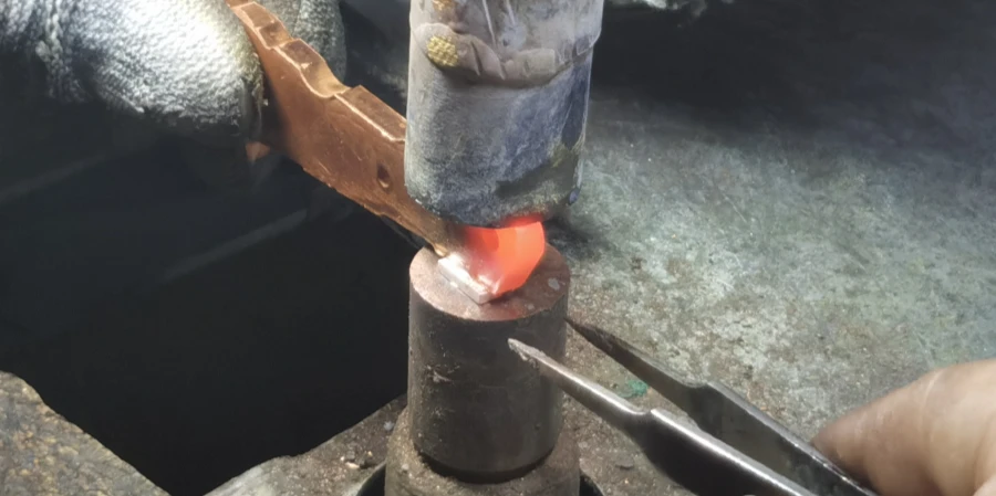 A person using pliers to hold a metal rod and heat it with a torch, brazing a silver contact onto the moving contact of a molded case circuit breaker, with the joint glowing bright orange