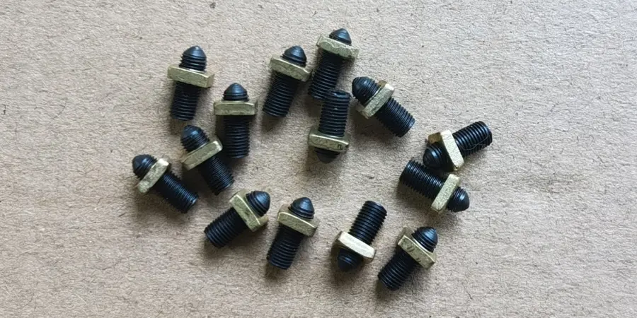 A group of black threaded calibration screws with pointed tips and attached metal washers, scattered on a gray textured surface, used inside a miniature circuit breaker.