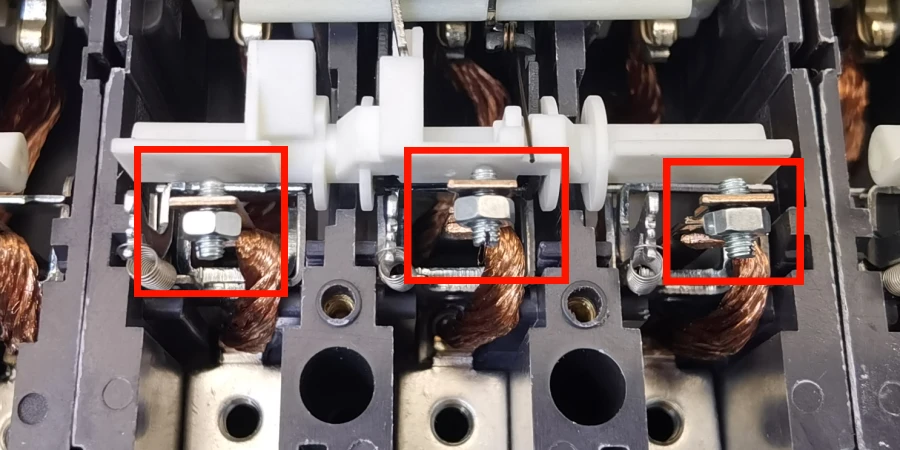 A close-up of mccb internals with three calibration screws highlighted in red boxes, each attached to a metal bracket and connected to braided copper wires, with a white plastic actuator bar above them.