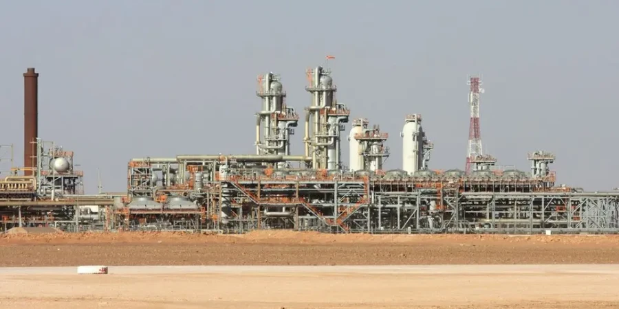 A gas power plant in Algeria with tall towers, pipes, and metal scaffolding, set in a flat desert landscape under a clear sky.
