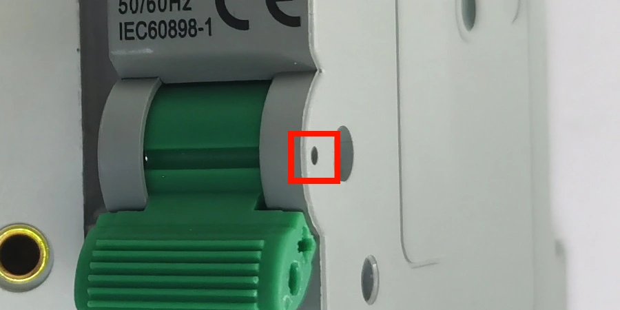 Close-up of an mcb with a red rectangle highlighting a small lockout hole next to a green switch