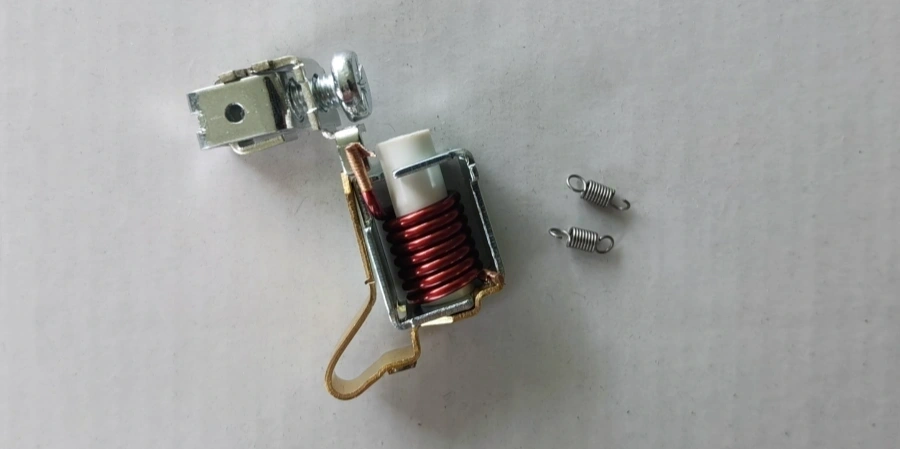An mcb internal coil assembly with a red copper coil and screw terminal, placed next to two small metal springs on a light surface.