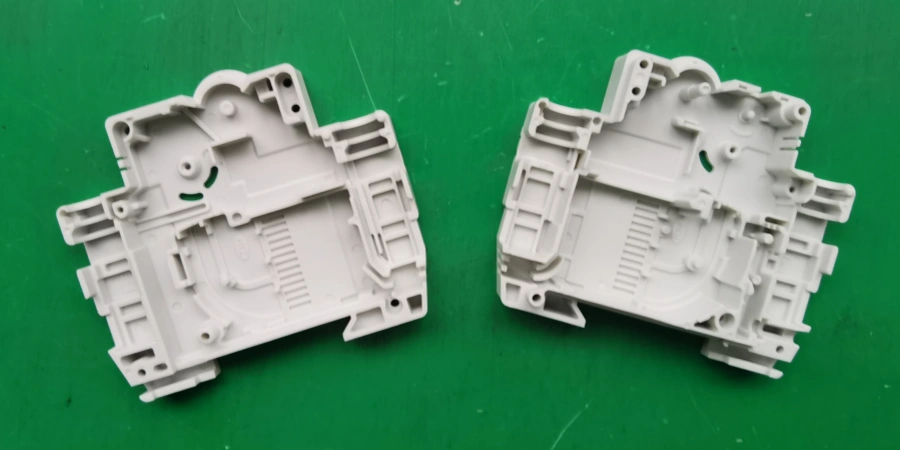Two white plastic miniature circuit breaker casings placed on a green background, showing internal molded details.