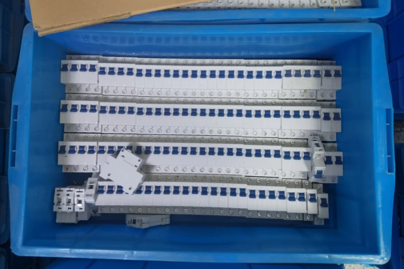 A blue plastic crate containing several rows of white miniature circuit breakers with blue switches, plus a few loose units scattered on top.