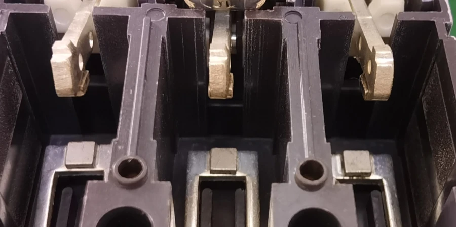Close-up view of the internal contacts of an MCCB, showing black plastic housings, fixed contact arms, and movable contact arms above them.