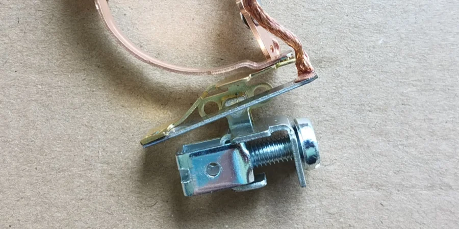 A close-up of a metal thermal trip assembly inside a miniature circuit breaker, featuring a brass bimetallic strip, copper wire, and a threaded adjustment screw on a gray surface.